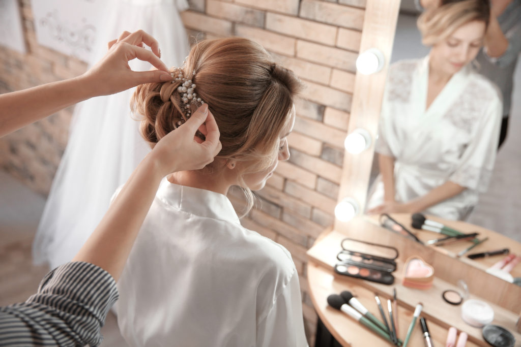 Photo of bride receiving wedding hair and makeup by a professional, updo is getting hair ornament.
