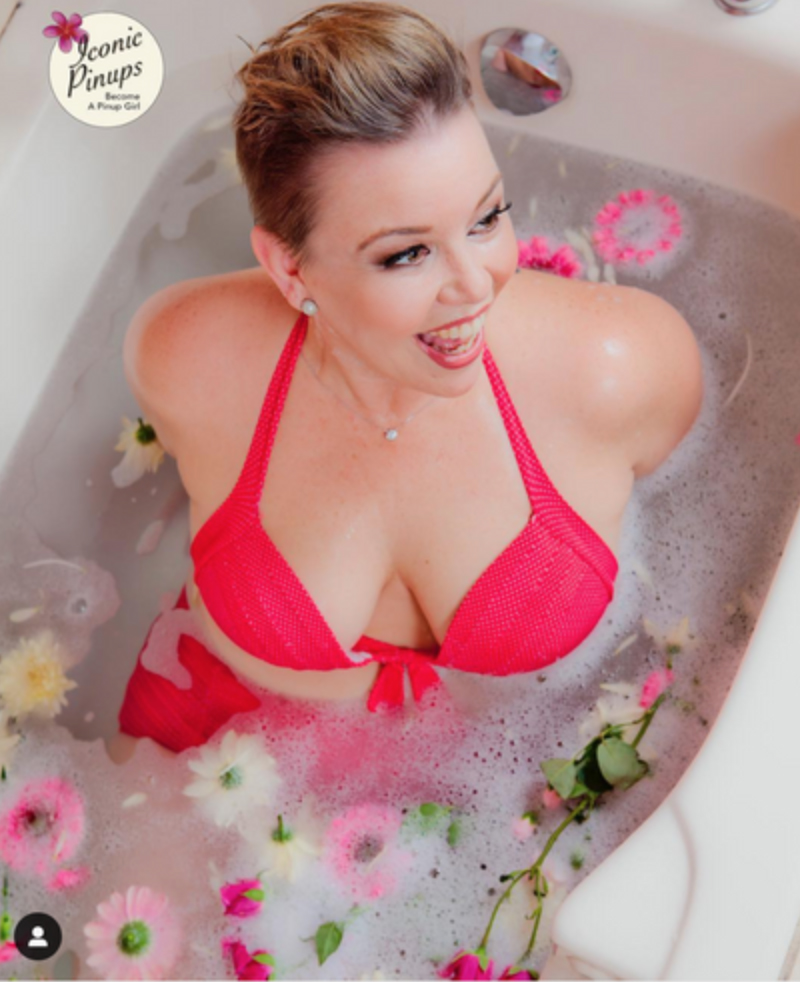 Beautiful girl in bathtub with flowers and bubbles floating in the water. She is wearing a red swimsuit.