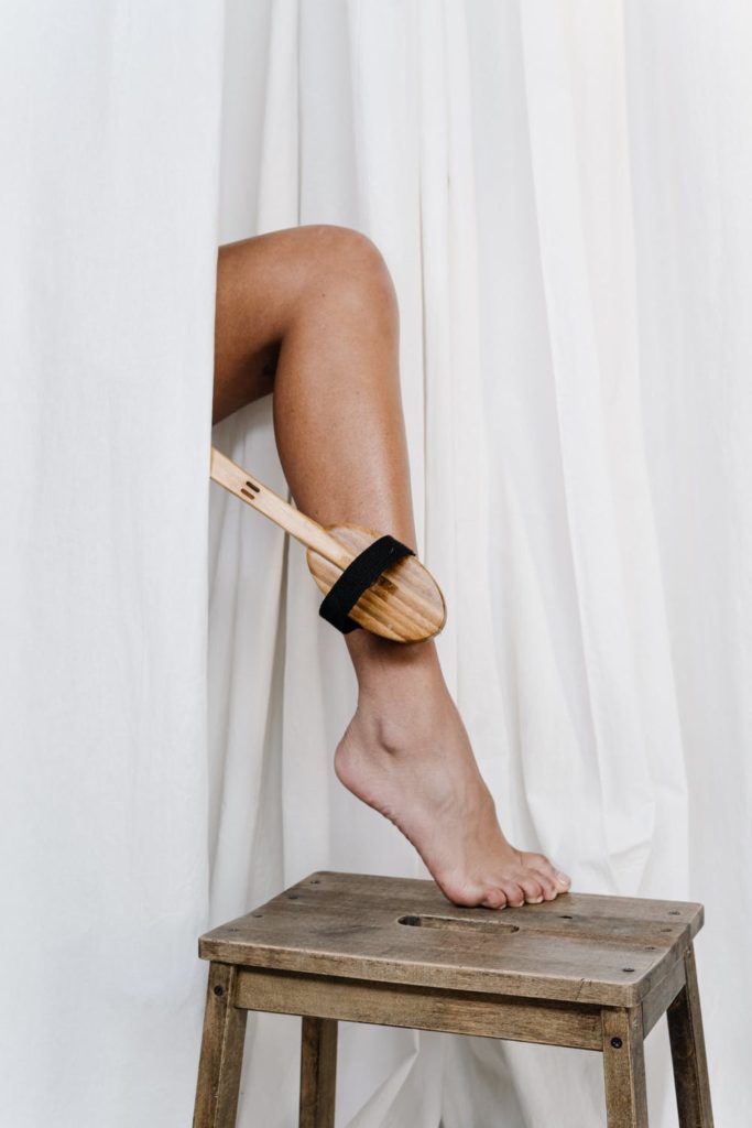 woman massaging her leg with a natural bristle brush to stimulate the lymphatic system.