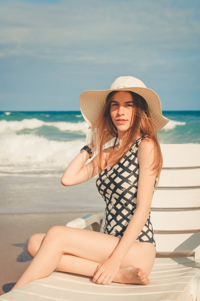 Beautiful young woman on the beach wearing a swimsuit and a big sun hat.